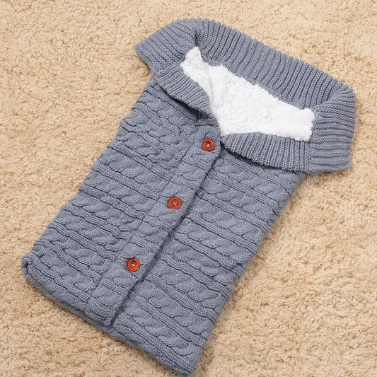 Gray knitted baby sleeping bag with white fleece inside lining and brown buttons with a ribbed neckline.